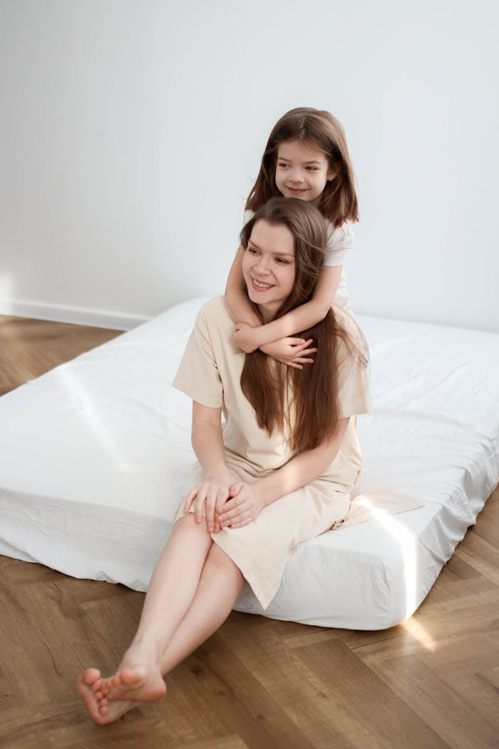 our-story-02 A mother and daughter share a joyful moment together on a bed, showcasing love and bonding.