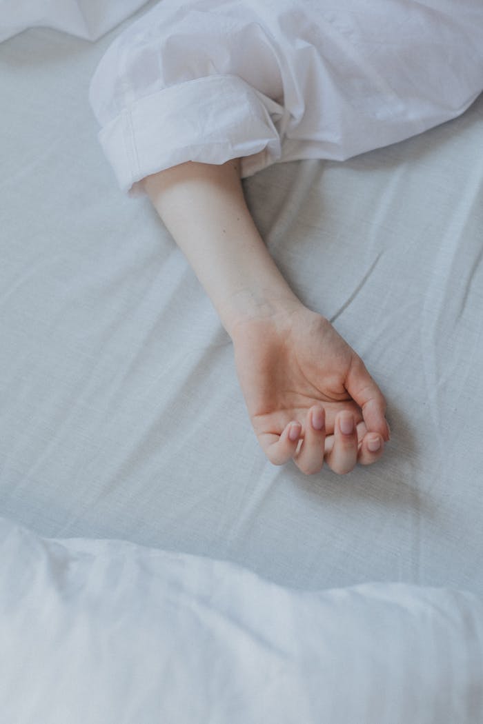 our-story-01 Close-up of a relaxed arm resting on a white bed sheet, suggesting tranquility.